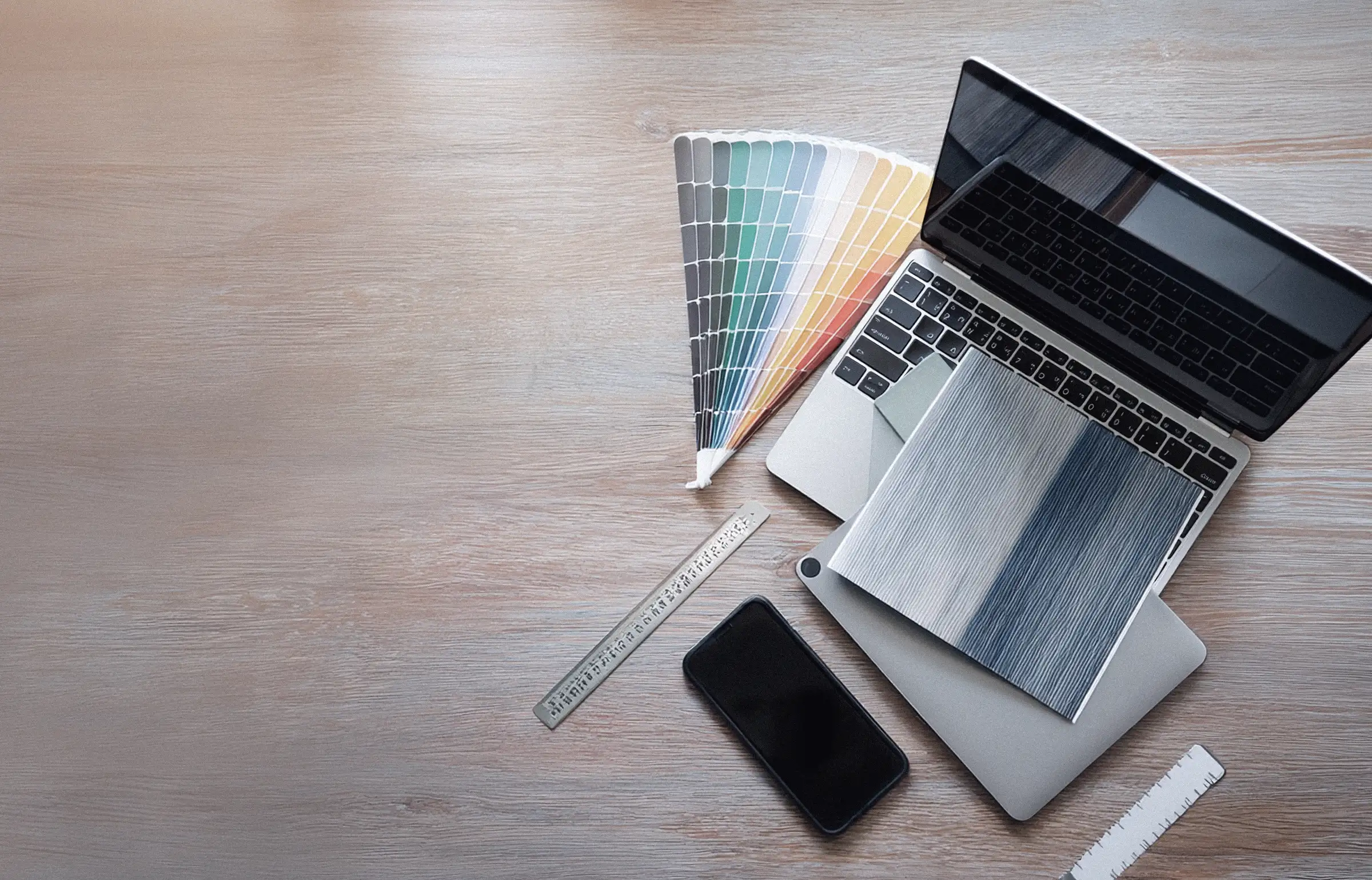 Mesa de trabajo de diseño web con un portátil, un muestrario de colores, un móvil y una regla