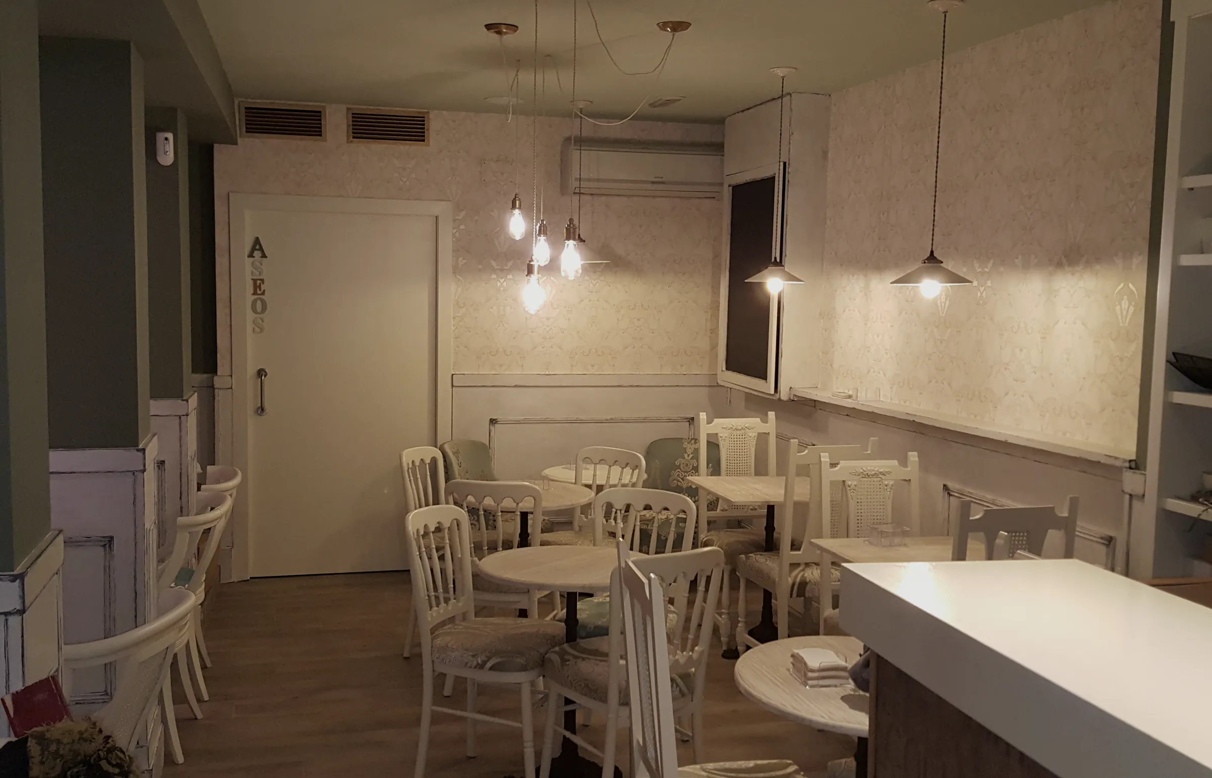 Sala de la cafetería La Crème con mesas y sillas blancas bajo lámparas colgantes