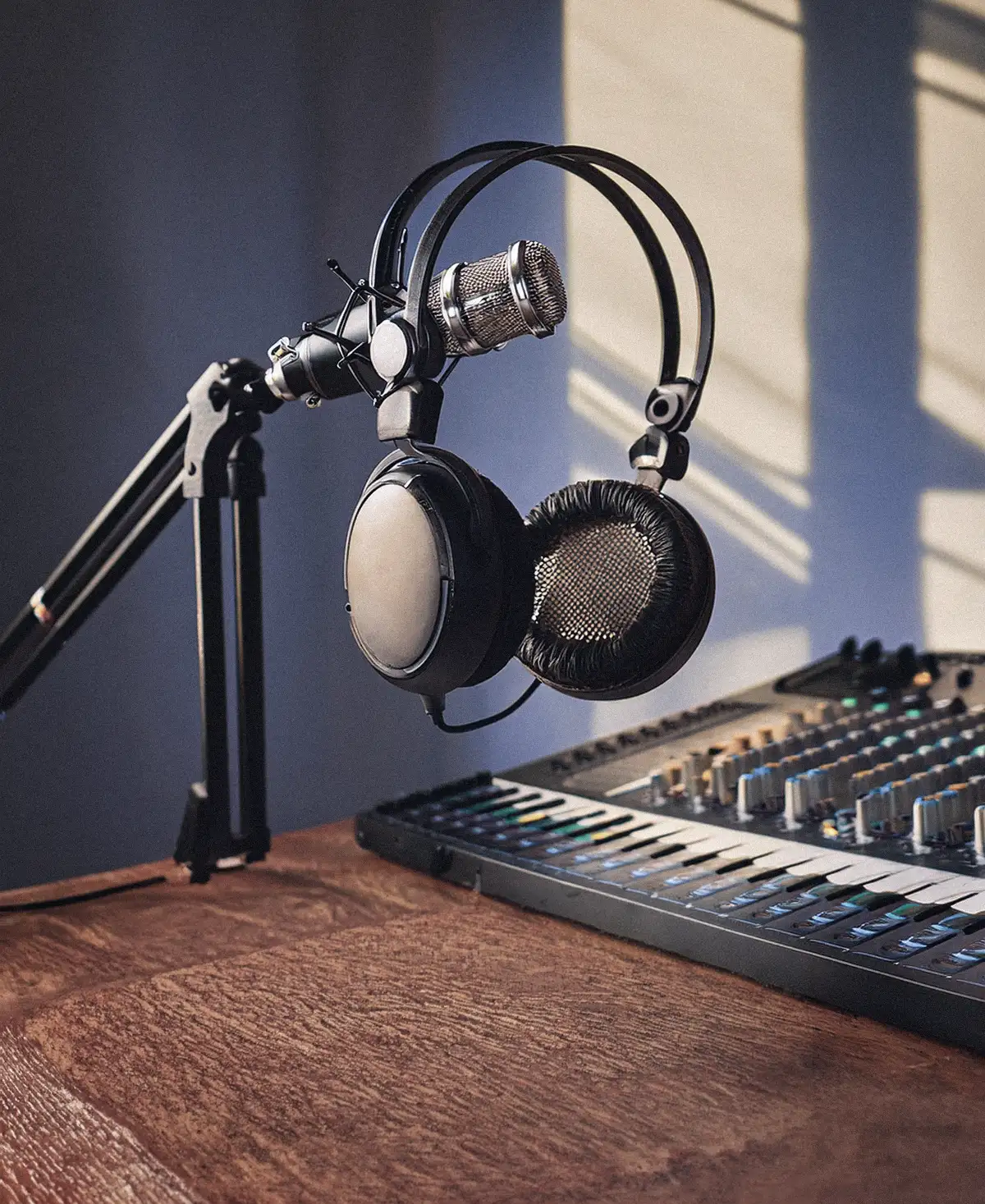 Auriculares de estudio colgados de un brazo de micrófono con una mesa de mezclas al fondo