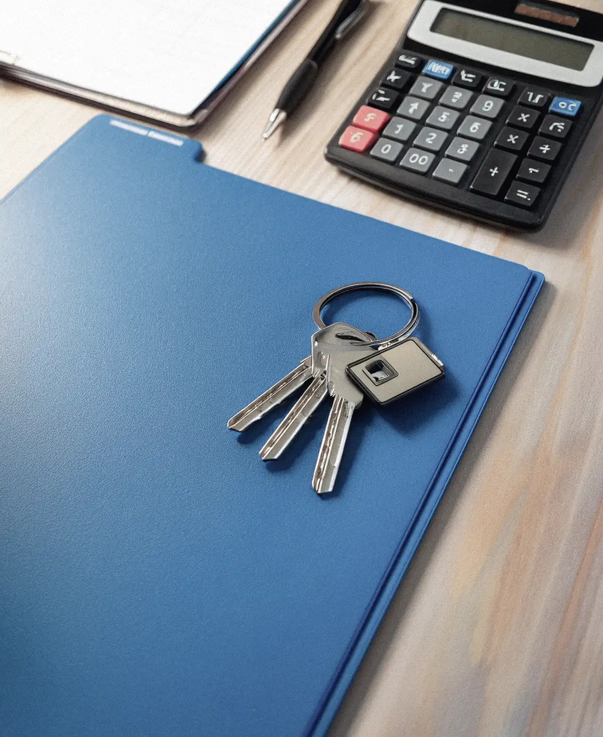 Llaves de una casa sobre una carpeta de documentos junto a una calculadora de sobremesa